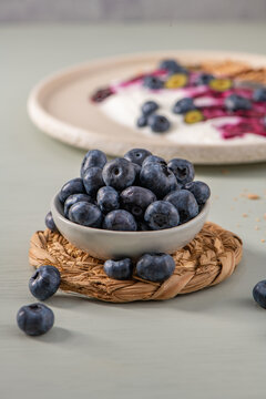 Fresh blueberries in a small bowl with a blurred yogurt breakfast dish in the background