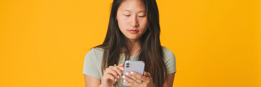Thoughtful girl in gray top scrolling on smartphone screen, looking at mobile phone, tap on screen while choosing something with indecisive expression