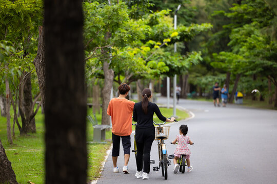Joyful Asian young girl while riding a bicycle with her grandfather in park on sunny day. girl kid on bicycles having fun in city park. outdoor activitie with daughter father mother and grandfather