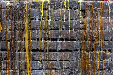 Obraz premium Melted colored wax dripping down rough brick wall, yellow and brown streams creating textured vertical patterns and weathered, layered surface with glossy drips and residue