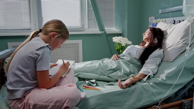 Girl calmly draws picture while mother rests in hospital ward