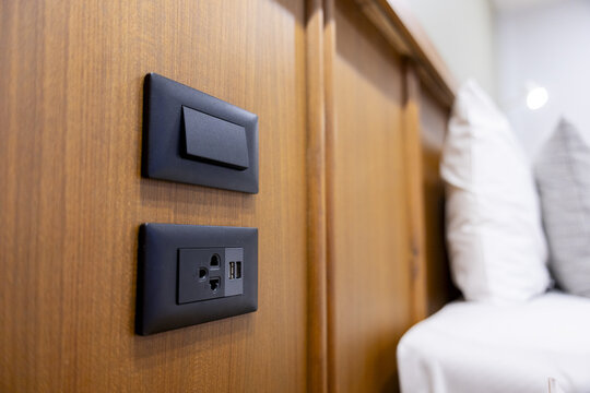 Modern bedside electrical outlet and light switch mounted on wooden headboard near bed pillows, convenient USB charging and universal socket for devices in cozy bedroom setting