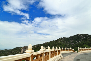 A beautiful outdoor viewpoint or terrace of an Asian temple featuring a decorative concrete railing with lotus-shaped finials. The curved observation deck overlooks a lush green rocky mountain range u © IZIFOTO