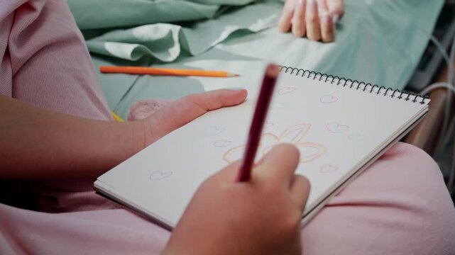 Close view shows girl drawing flower for mother in hospital