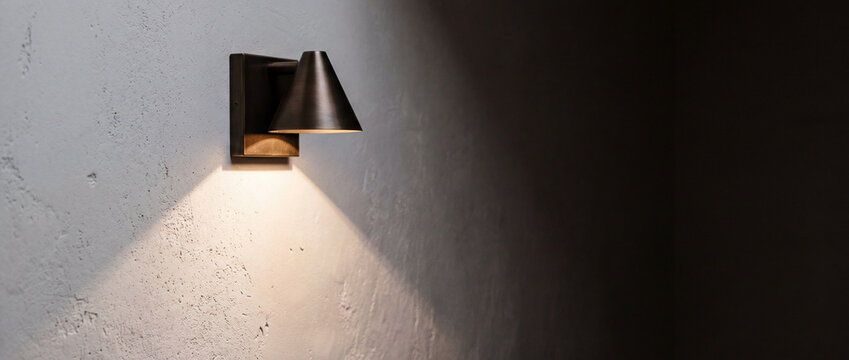 Minimalist wall sconce casting warm light and shadow on textured interior wall, moody home lighting