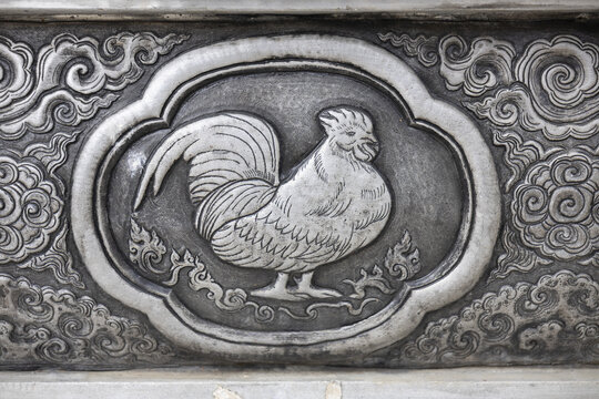 Silver bas relief panel depicting rooster in ornamental cloud frame, detailed metalwork with engraved feathers and swirling decorative motifs conveying calm elegance