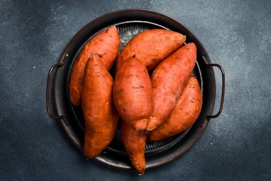 Close up of raw organic sweet potatoes. On a tray. Gray stone background.