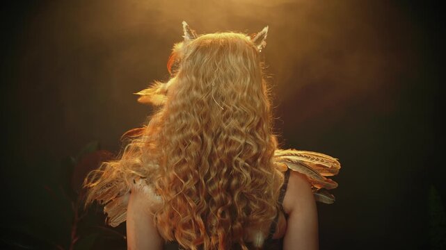 fantasy woman owl bird costume brown natural feathers ears horns. Creative halloween holiday makeup, beautiful face eyes lips, blonde long curly hair. fairy tale shaman voodoo elf girl looking back 