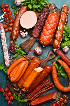 Set of different types of sausages, salami, pepperoni and smoked sausages with basil and spices on a concrete background. Top view. Vertical photo.