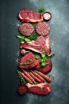 Set of meat and meat products. T-bone steak, ribeye steak, kebab and burger patty. On a black stone background. Top view.