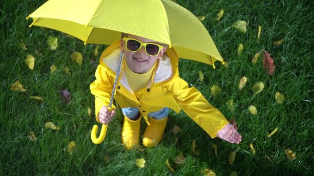 A happy child plays outside in an autumn park. A child with a yellow umbrella enjoys the autumn rain. Slow motion