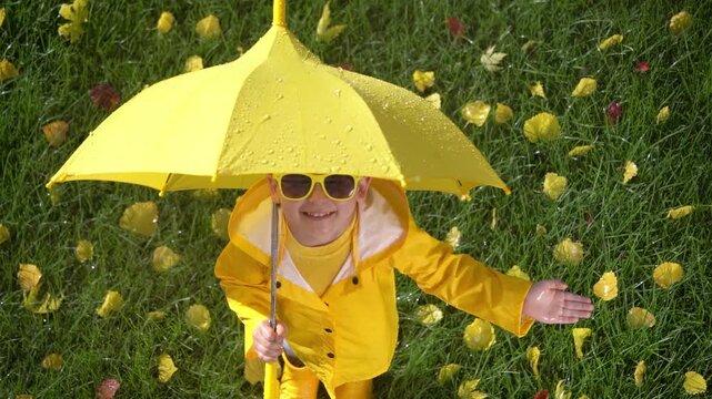 A happy child plays outside in an autumn park. A child with a yellow umbrella enjoys the autumn rain. Slow motion