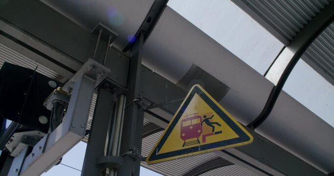 Yellow warning sign at a train station depicting a person falling towards a train