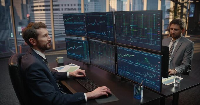 Portrait of Stockbrokers Reviews Trading Data Across a Multi-screen Desk Setup, Smiling as He Monitors Financial Charts, Investment Portfolios, and Capital Growth in an Office. Elevated Shot