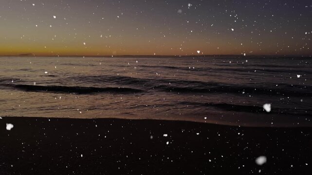 Snow falling over a calm sea at sunrise with gentle waves and golden morning light.