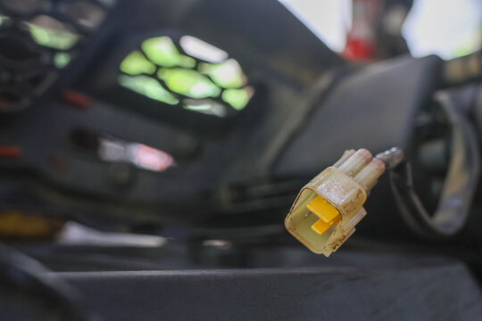 Yellow plastic electrical connector hanging from wire motorcycle frame with shallow depth of field, close up showing worn insulation and metal terminal, gritty workshop atmosphere with soft bokeh