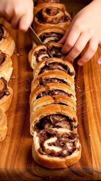 Hands slicing homemade chocolate babka roll on wooden board.