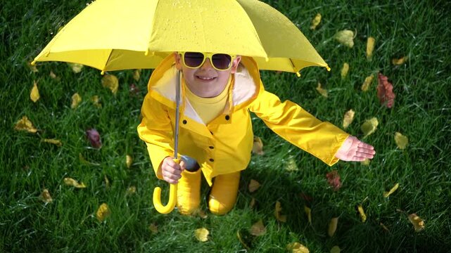 A happy child plays outside in an autumn park. A child with a yellow umbrella enjoys the autumn rain. Slow motion