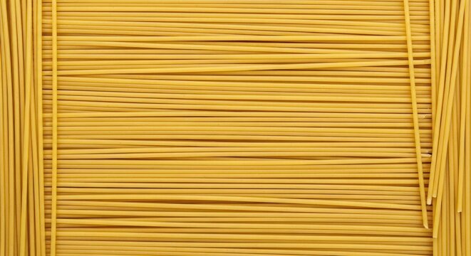 A stack of long, golden-yellow spaghetti noodles is arranged horizontally against a black background. The noodles are tightly packed, creating a textured surface.