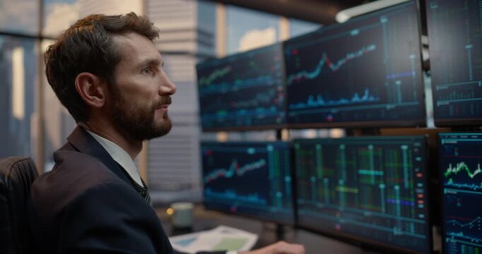 Portrait of Male Stock Trader Reviews Market Data Across a Multi-screen Desk Setup, Evaluating Financial Charts, Ticker Indices and Investment Portfolios to Strategize Capital Growth and Profit.