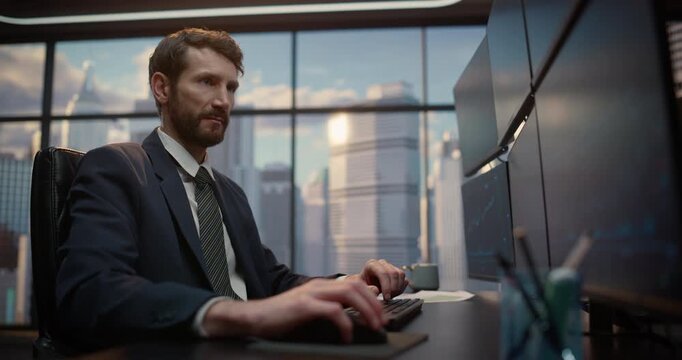 Stockbroker Types Financial Commands at His Desk, Monitoring Exchange Data and Investment Portfolios on Computer Computer Screens to Analyze Market for Wealth Growth. Low Angle Portrait