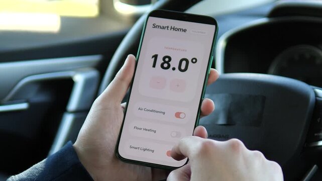 Driver using a smartphone app to pre-cool the house before arrival. Screen shows active AC and lighting settings. High demand for remote living, digital assistants, and connected home stock video.