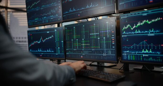 Over-the-shoulder View of a Male Trader Working at a Multi-monitor Desk Displaying Stock Exchange Data, Equity Charts and Market Analytics for Investment, Capital Growth. Asset Management Company