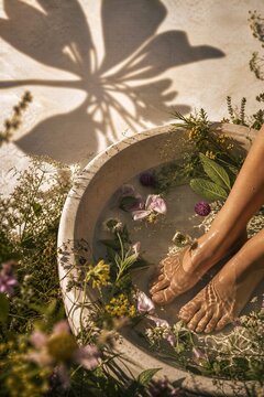 Woman soaking feet in stone basin filled with water and aromatic herbs. Natural spa treatment and herbal therapy for relaxation. Wellness, beauty care and meditation in summer garden