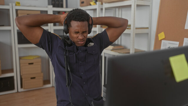 Man police in uniform wearing headset with hand to mouth for cough then raises arms at desk in building; exhaustion duty.