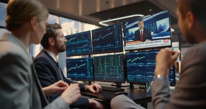 Team of Brokers Watch Financial TV News Channel and Live Stock Exchange Data at a Desk With Multiple Monitors, Analysing Equity Charts and Broadcast Feeds to Debate Investment Strategy, Market Trends