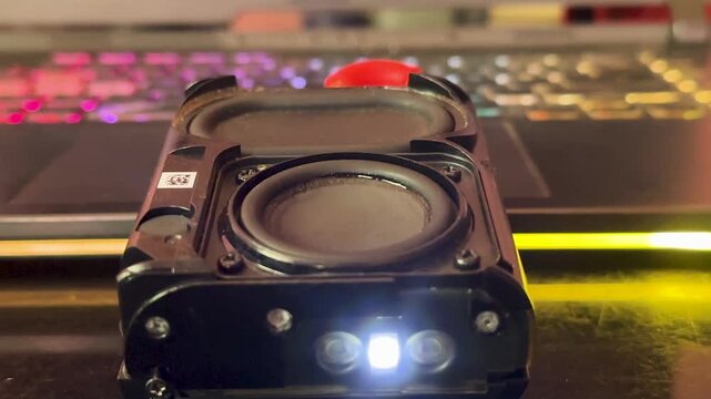 Small portable bluetooth speaker vibrating while playing loud music with colorful led lights background.