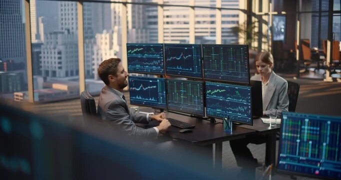 Successful Male Trader Celebrates Winning Investment With Raised Fists at Multi monitor Desk Showing Stock Exchange Data, Female Colleague Analyzes Market Charts and Financial Analytics.
