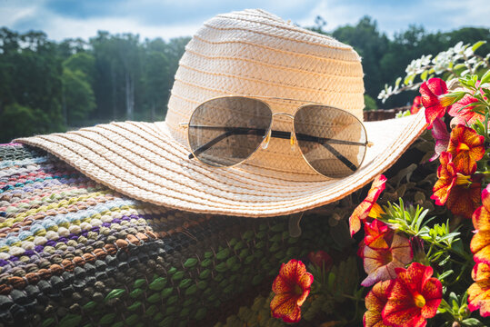 Straw sun hat with aviator sunglasses surrounded by vibrant blooming flowers under a blue summer sky. Stylish seasonal still life for travel, vacation and outdoor lifestyle concepts.
