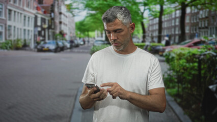 Fototapeta premium Middle age man with grey hair holds smartphone to ear on a cobbled city street, forearm exposed while talking into phone; concern waiting urgency.