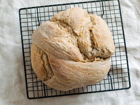 Freshly baked artisan sourdough knot bread loaf cooling down on a black metal wire rack. Top down overhead view on a rustic wooden table background. Perfect for baking process and bakery concept