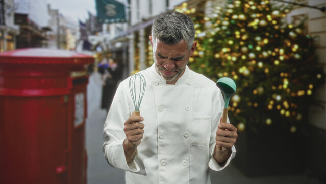 Chef holds whisk and ladle, winces with closed eyes on a busy street beside a decorated christmas tree and red postbox; holiday stress.