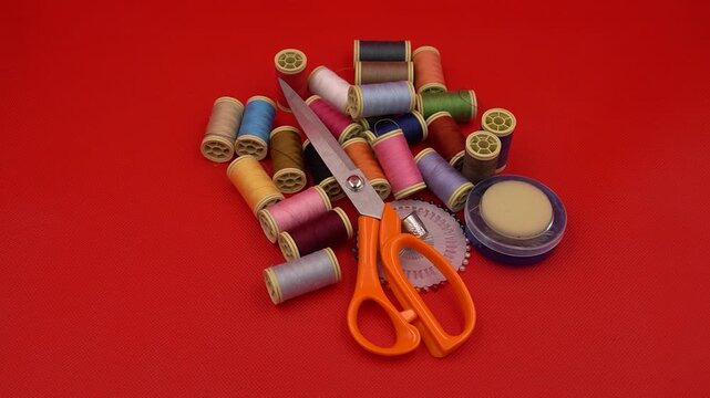 Colorful Sewing Supplies with Threads, Scissors, and Measuring Tape on a Red Background
