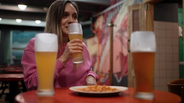 Friends at beer garden laugh drink beer and eat burgers. Golden hour sunset light. Young women enjoy outdoor meal, social gathering, casual meeting, outdoor dining
