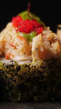 Sushi rolls with tobiko caviar on black platter, closeup. Japanese cuisine . Vertical footage