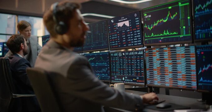 Portrait of Stockbroker in Monitors Stock Exchange Data, Investment Analytics, Capital Growth Charts on Desk Computer Screens as Team Colleagues Talk in Trading Office. Asset Management Company