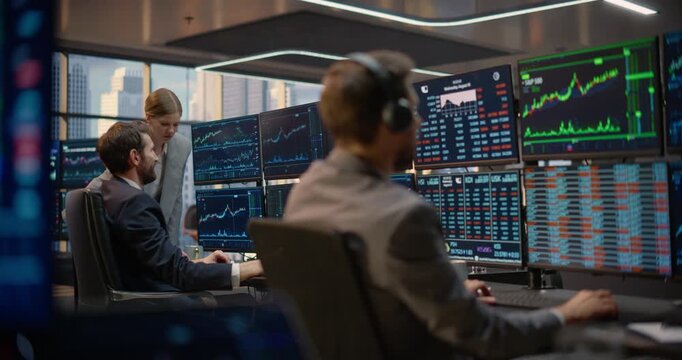 Stockbrokers Discuss Stock Exchange Data and Investment Analytics at a Trading Desk as a Female Broker Points at Capital Growth Charts While a Headset Trader Monitors Market Computer Screens Nearby