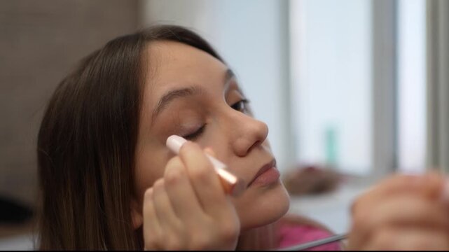 Woman applying light eyeliner or concealer to her eyelid in front of a mirror. Eye makeup, beauty routine, and cosmetic enhancement.