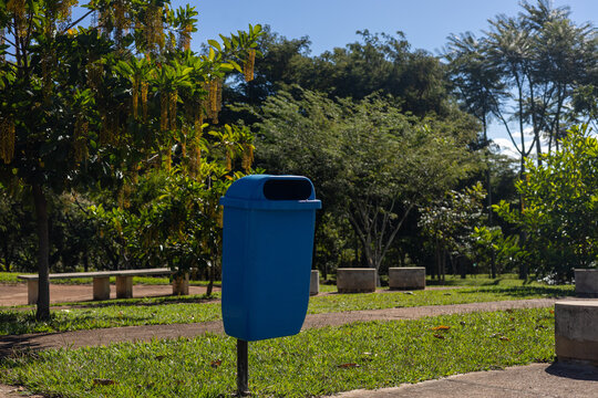 Cesto de lixo azul em parque p&uacute;blico arborizado e ensolarado / Blue trash can in a sunny, wooded public park
