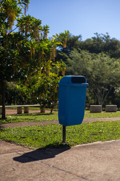 Cesto de lixo azul em parque p&uacute;blico arborizado e ensolarado / Blue trash can in a sunny, wooded public park