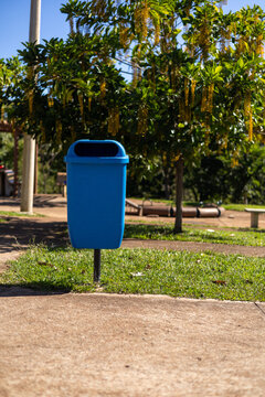 Cesto de lixo azul em parque p&uacute;blico arborizado e ensolarado / Blue trash can in a sunny, wooded public park