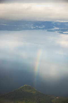 Rainbow arc bending over forest hill and lake