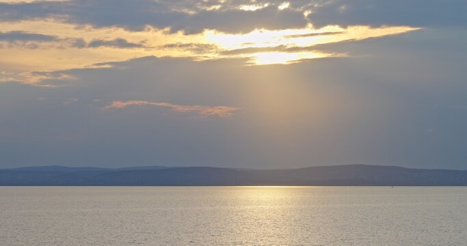 Sun setting over calm lake water and distant mountains
