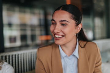 Fototapeta premium A smiling young businesswoman engages with colleagues during a remote work meeting. She chats comfortably in a modern office setting.