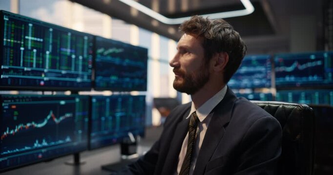 Portrait of Confident Male Trader turning and Looking at Camera while working at an Asset Management Firm. Investment Strategy, Live Stock Exchange Screens, Corporate Career Success and Banking