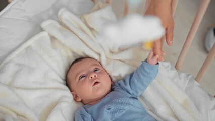 Newborn hispanic boy grasps an adult finger in a crib building, hand curled on a soft blanket, eyes focused upward  calm gentle bonding. © Krakenimages.com